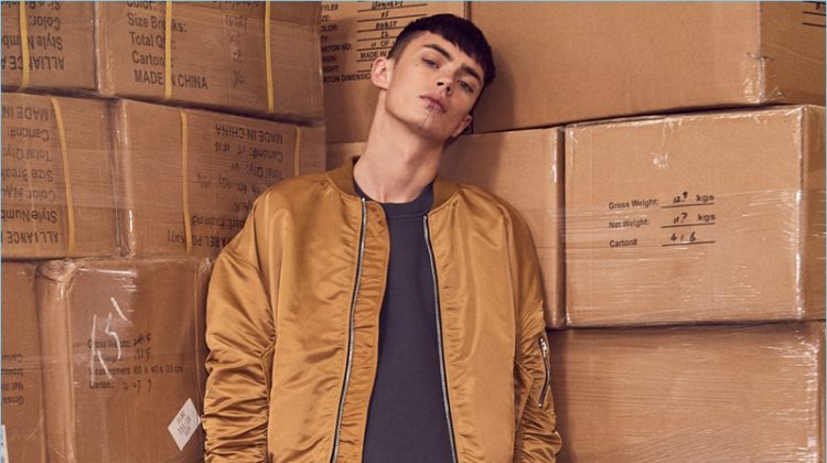 Model Simon Kotyk sports a typical streetwear look with a Fear of God bomber jacket, sweatshirt, and nubuck leather military sneakers. Simon also wears Mr. Completely denim jeans.