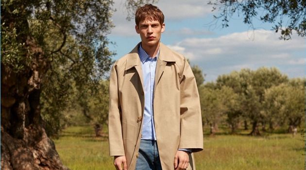 French model Baptiste Radufe dons a Mackintosh trench coat with a striped Commes des Garçons Shirt striped shirt. His look is complete with Balenciaga jeans and AMI shoes.