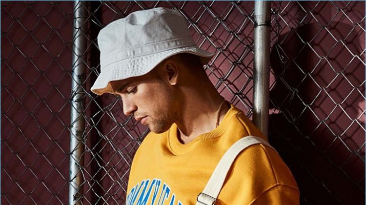 Embracing 90s style, River Viiperi wears LE 31 overalls with a yellow Tommy Jeans sweatshirt. The model also rocks an Adidas Originals bucket hat.