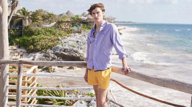 Embracing summer style, Tim Dibble wears a Lanvin striped shirt, Marané swim shorts, and a logo charm necklace by Saint Laurent.