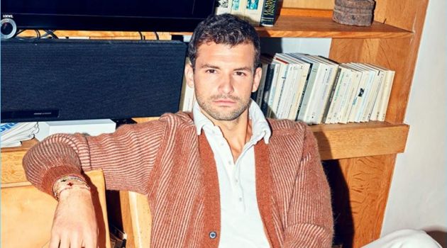 Relaxing, Grigor Dimitrov sports a Lanvin cardigan, Massimo Alba polo, and white Burberry jeans.