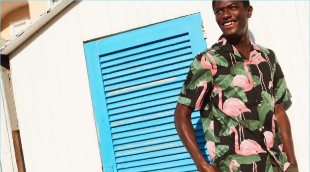 Hamid Onifade reunites with H&M. He wears a relaxed fit flamingo print shirt with cargo shorts.