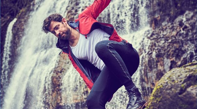 Actor John Krasinski wears a Z Zegna windbreaker, Calvin Klein tank, New Balance joggers, American Trench socks, a Breitling watch, and David Yurman necklace.