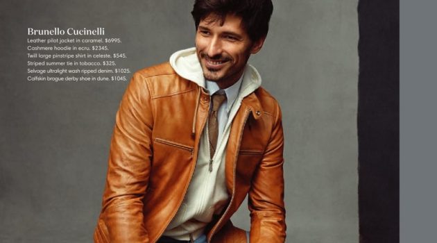 All smiles, Andres Velencoso dons a Brunello Cucinelli caramel leather jacket, cashmere hoodie, pinstripe shirt, striped tie, ripped jeans, and brogue derby shoes.