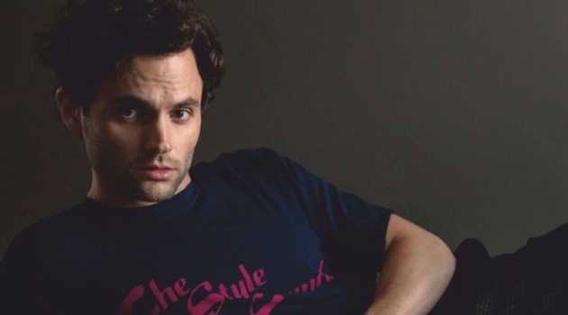 Posing for a studio photo, Penn Badgley wears an Opening Ceremony t-shirt, Bally trousers, and COS shoes.