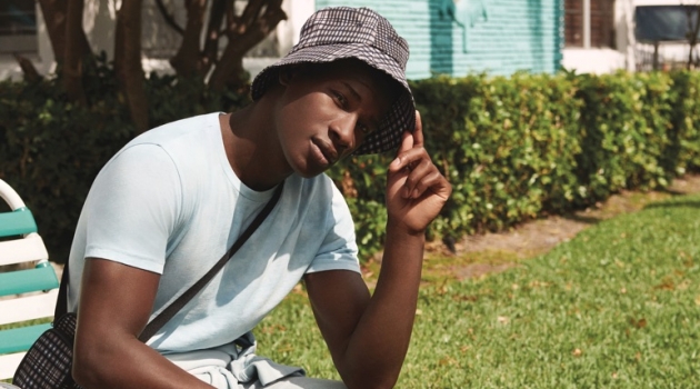 Connecting with River Island, David Agobdji sports a summer look, complete with a plaid bag and bucket hat.