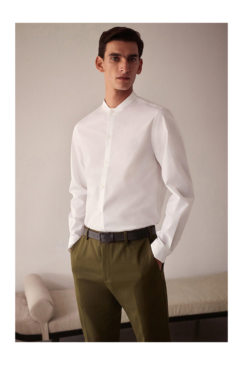 Embracing minimal style, Thibaud Charon models a white band-collar shirt with trousers from COS.