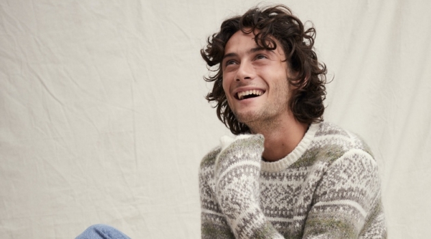 All smiles, Oli Green sports a fairisle sweater with light wash denim jeans from Alex Mill.