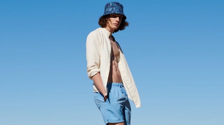 Sporting a bucket hat with a yellow top and blue swim shorts, Pawel Feledyn wears Reserved.