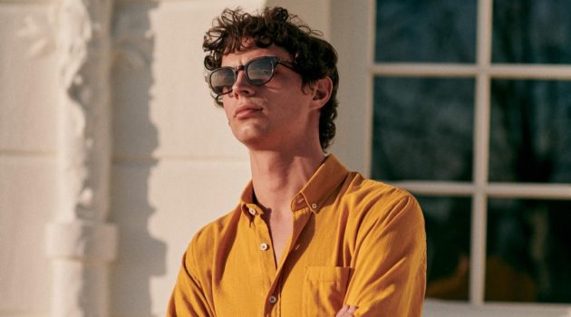 Dressing for warm weather, Andrea Quaranta models a mustard yellow shirt with striped swim shorts and stylish sunglasses by Octobre.