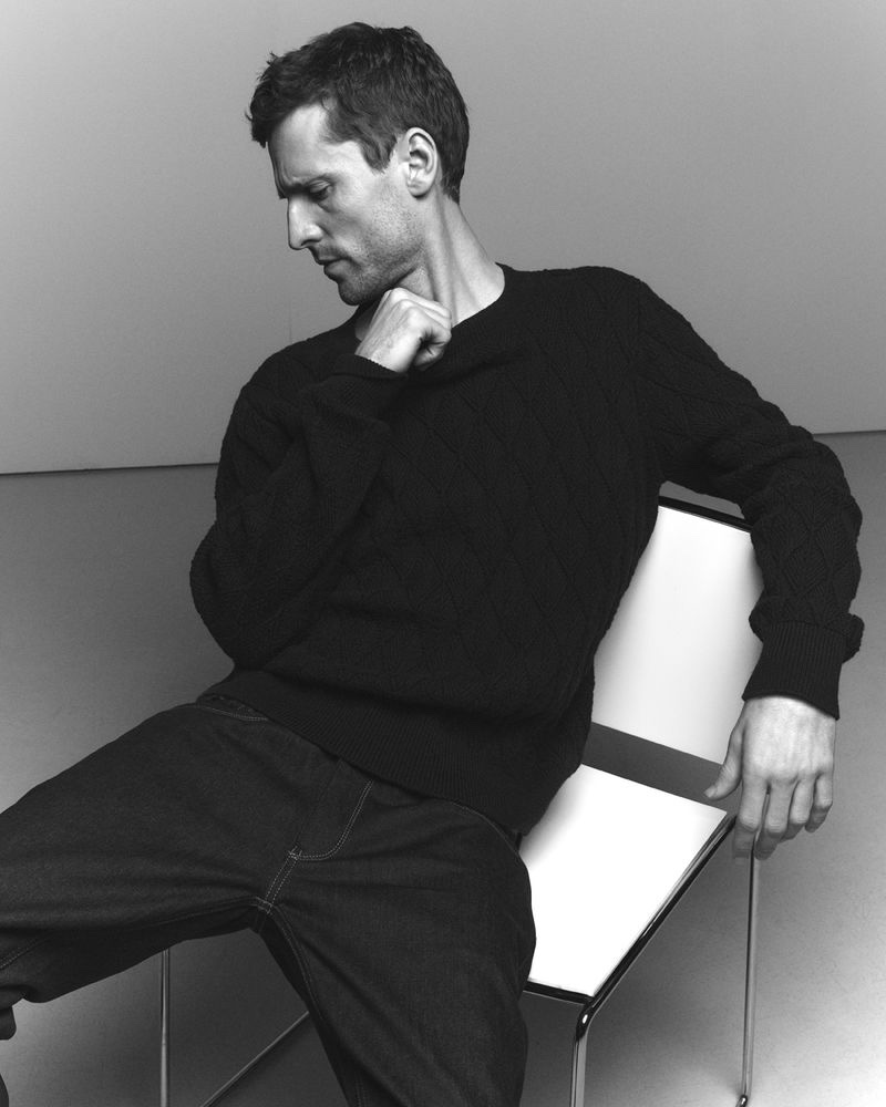Sitting for a black-and-white photo, George Barnett dons a crewneck sweater and denim jeans for DENHAM's fall-winter 2023 campaign. 