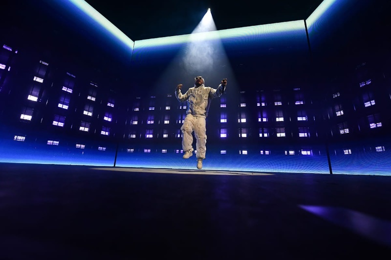 J Balvin levitates mid-air against a backdrop of geometric light panels at the G-SHOCK 40th anniversary event. 