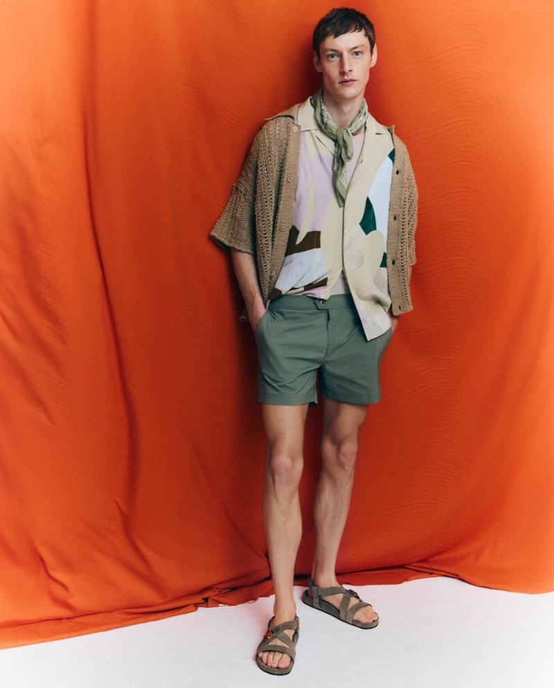 Embracing a smart summer look, Roberto Sipos models a Bonsai knit shirt, a JACQUEMUS graphic shirt, Tom Ford swim shorts, and Wales Bonner sandals. 
