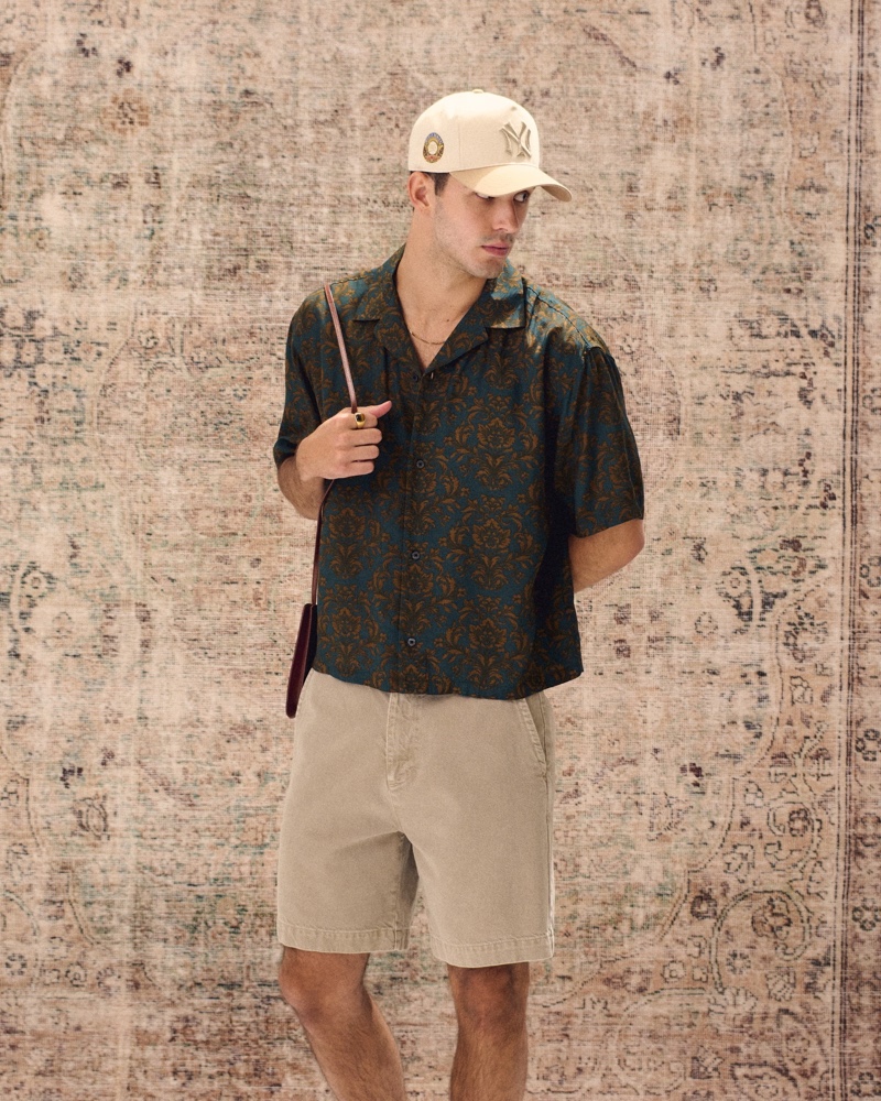 Abercrombie & Fitch proposes a laid-back summer style with its dark green camp collar silky shirt, light brown denim shorts, and New York Yankees '47 Clean-Up hat.