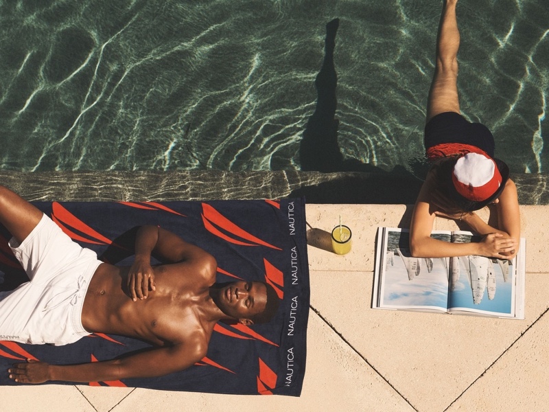 Henry Watkins relaxes poolside in white swim shorts for Nautica's summer 2024 campaign.