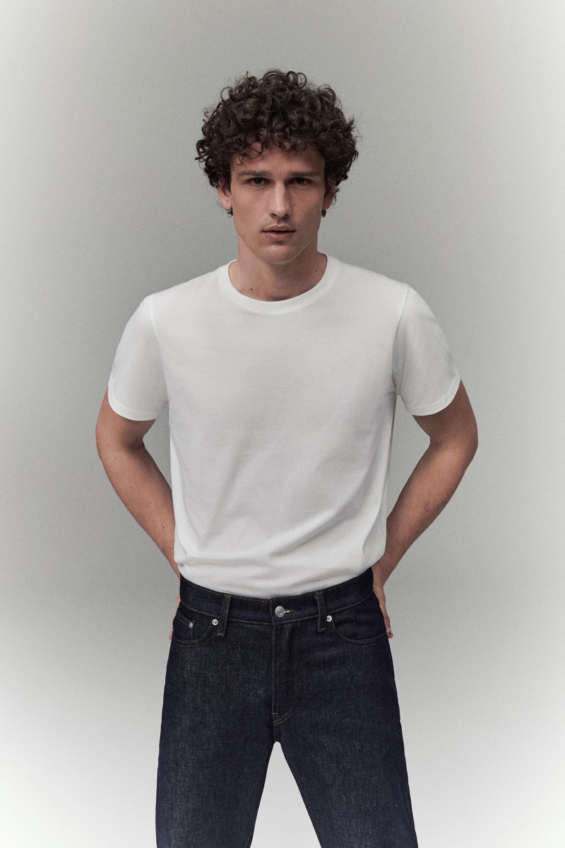 Simon Nessman wears a classic white t-shirt with dark rinse denim jeans.