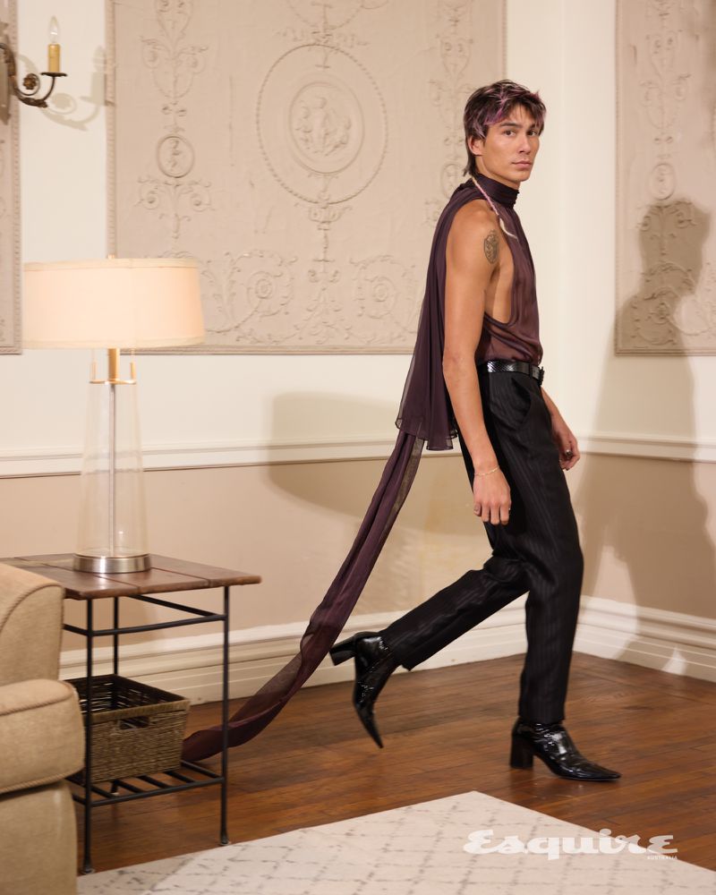 Walking through a richly decorated room, Evan Mock wears a sleeveless top and fitted trousers by Saint Laurent.