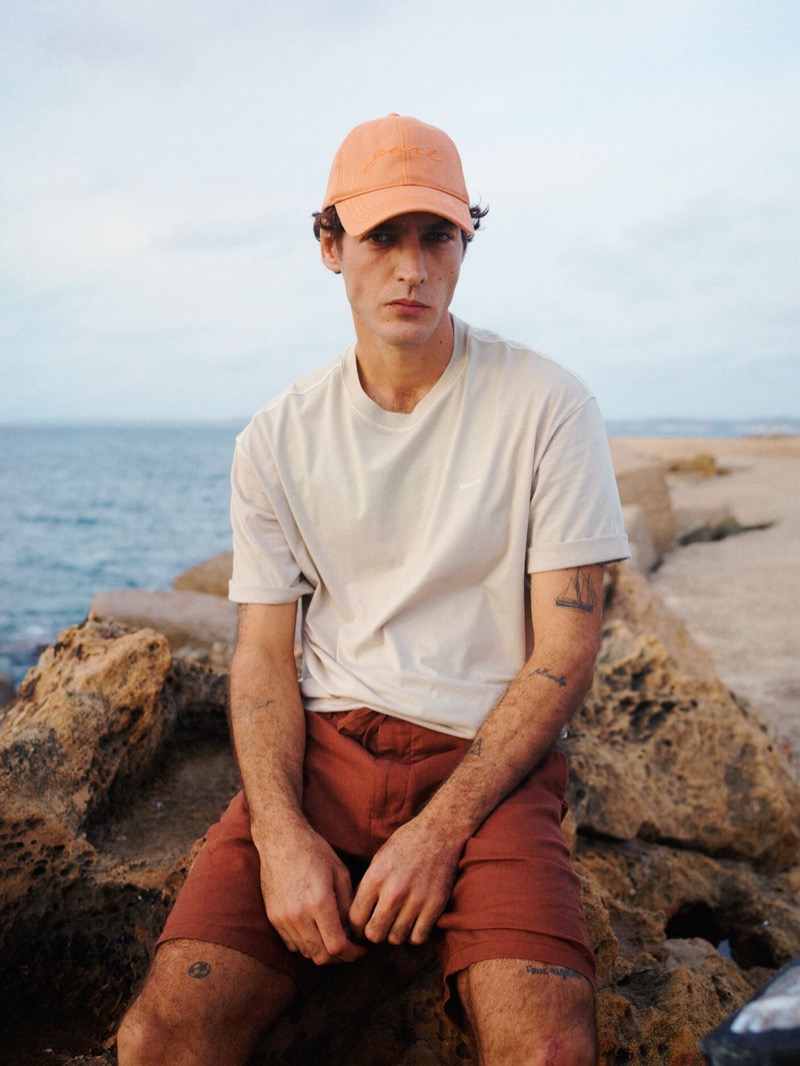 At the seaside, Pierre-Benoit Talbourdet sports a relaxed look with a cap, beige tee, and shorts from GANT's summer 2024 collection.