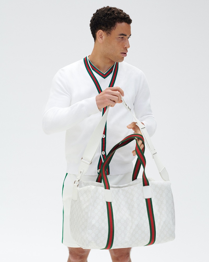 George Loffhagen showcases Gucci's tennis collection, wearing a white ensemble with the brand's signature red and green web detailing, complemented by a matching duffle bag.
