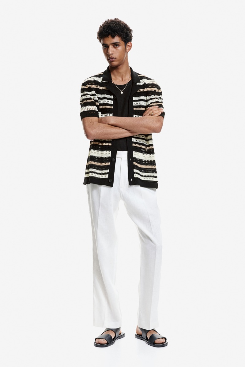 H&M's summer 2024 collection features a crochet-look resort shirt over a black knit tank top paired with white, relaxed-fit trousers.