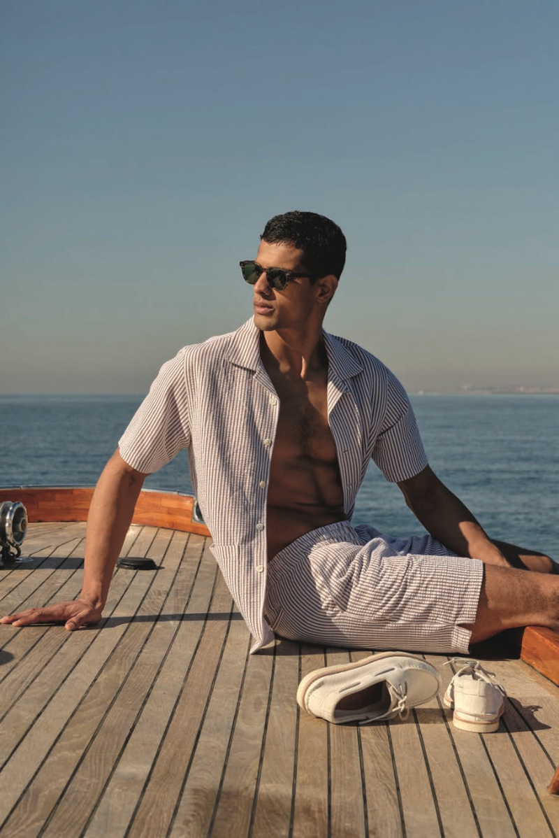 On the deck, Jonas Barros embraces nautical vibes in a seersucker Guayabera polo shirt and matching coach shorts, accessorized with Sperry Top Spider x Todd Snyder ivory footwear.