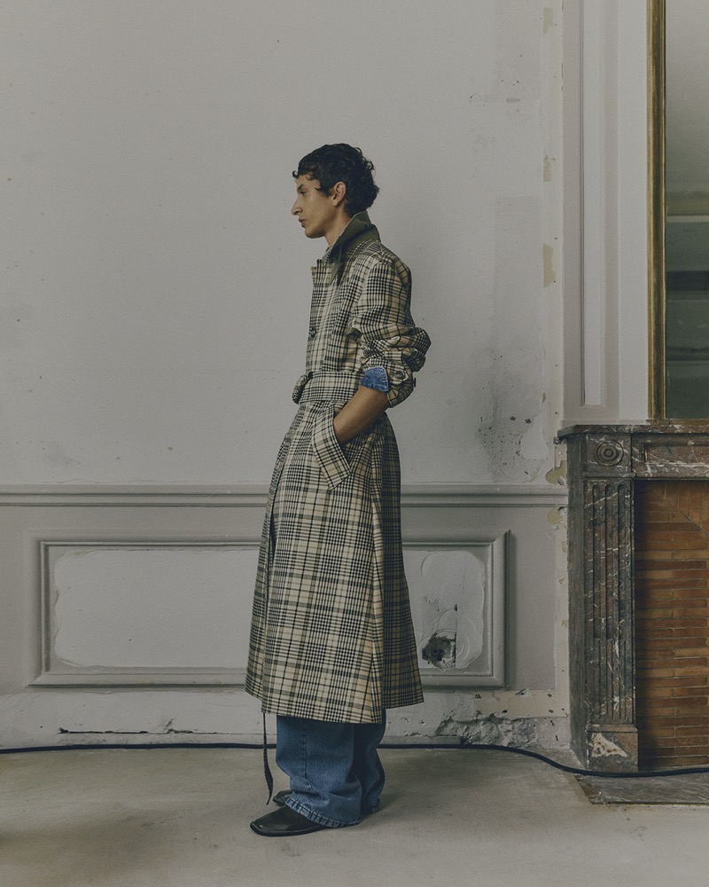 Takfarines Bengana stands poised in a checkered trench coat and jeans from AMI’s spring-summer 2025 collection.