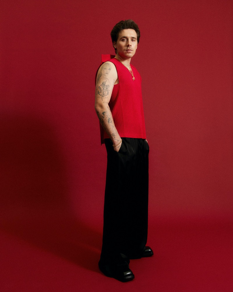 Connecting with InStyle, Brooklyn Beckham dons a sleeveless red Homme Plissé Issey Miyake top with black Giorgio Armani trousers and Prada shoes.