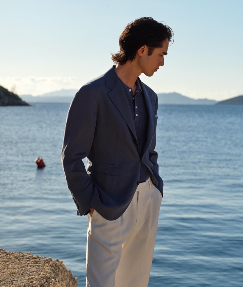 By the seaside, Peter Meyer models a navy blazer paired with cream trousers, showcasing the timeless elegance of Brunello Cucinelli’s high summer 2024 collection.