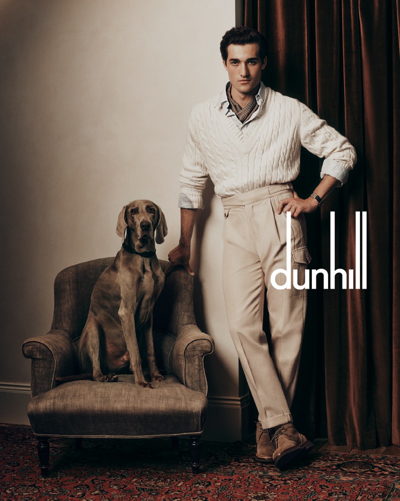 Adam Sattrup embraces a refined look for Dunhill’s fall-winter 2024, featuring a cable-knit sweater and high-waisted cargo trousers complemented by a loyal canine companion.