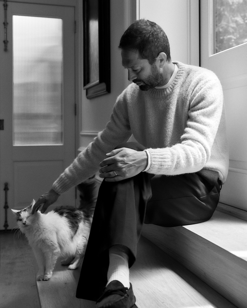 In a quiet moment with his cat Sonny, Ebon Moss-Bachrach dons Tom Ford’s alpaca-blend sweater, paired with Acne Studios’ straight-leg twill trousers and The Row’s suede driving shoes.