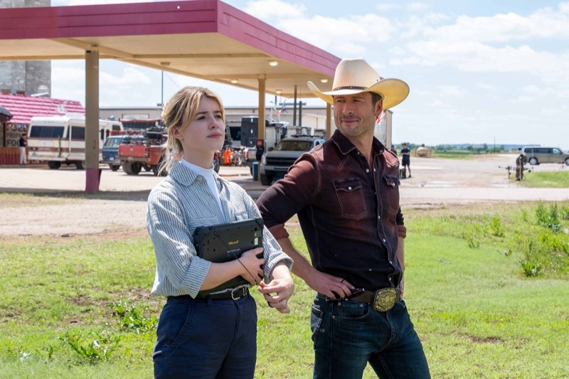 Glen Powell, as Tyler Owens, stands beside Daisy Edgar-Jones’ Kate Carter, sporting a classic cowboy hat and a rugged denim ensemble in “Twisters.”