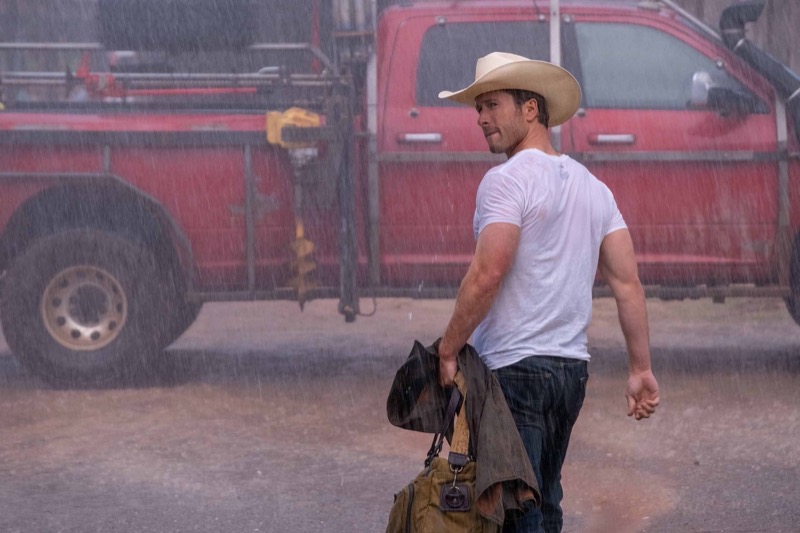 Tyler Owens, played by Glen Powell, strides through a downpour in a white tee and cowboy hat in “Twisters.”