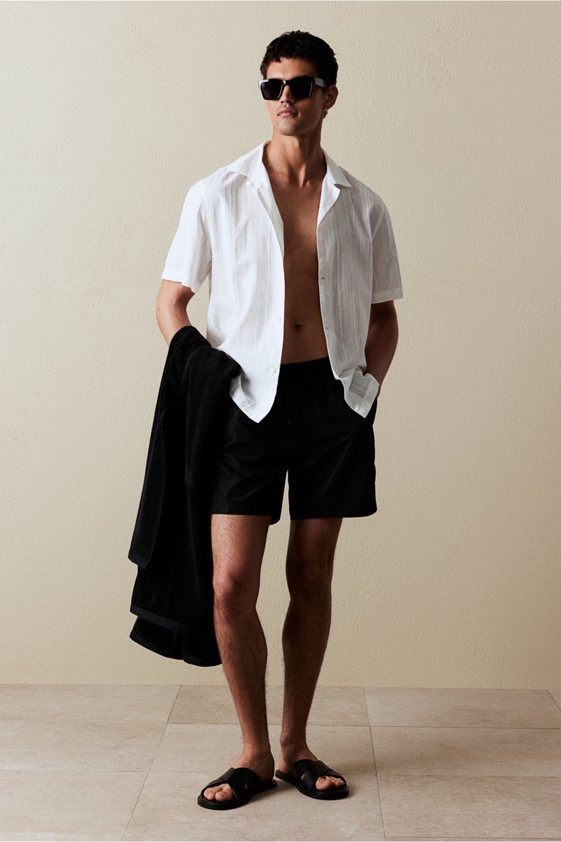 Model Bodhi Heeck wears a white and black swim shorts outfit. 