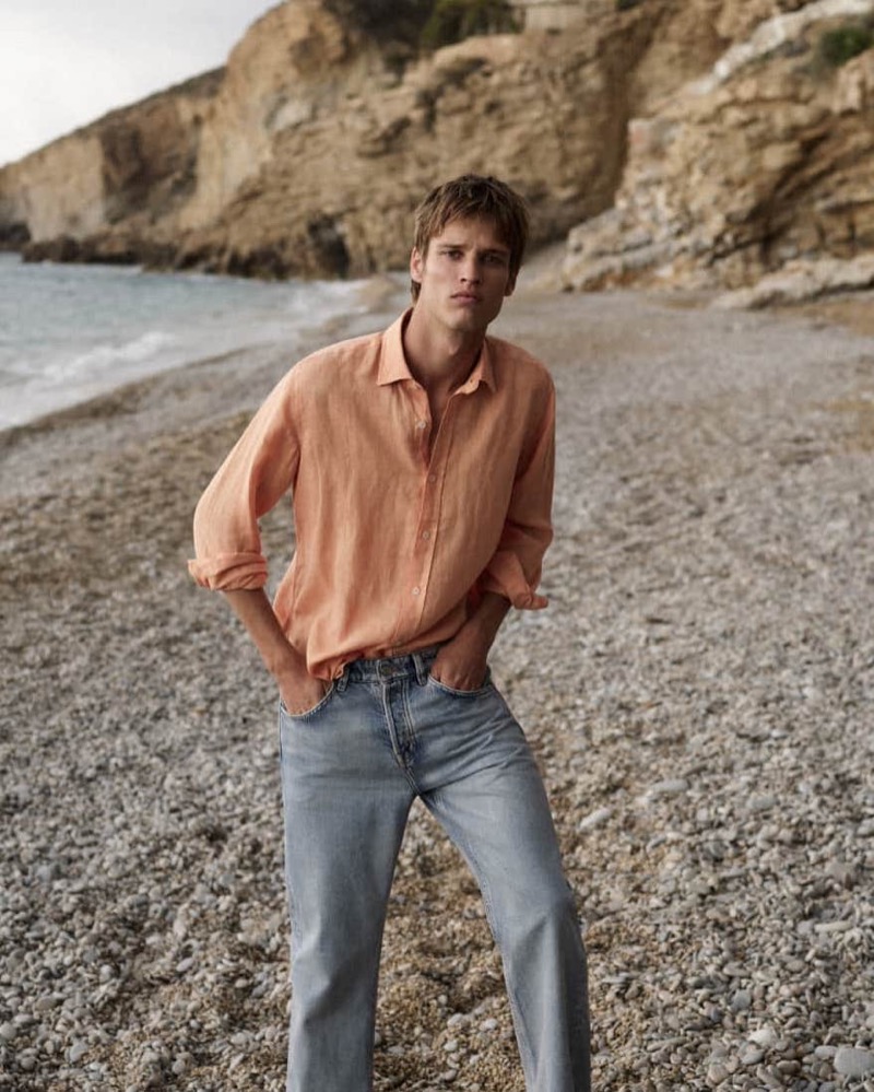 On a pebbled beach, Yeray Allgayer dons Massimo Dutti’s breezy peach shirt with light-wash jeans. 