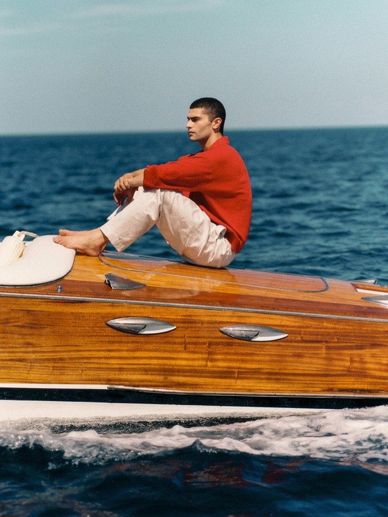 Sitting atop a speedboat, Charlie Knepper wears a red Massimo Dutti sweater polo.