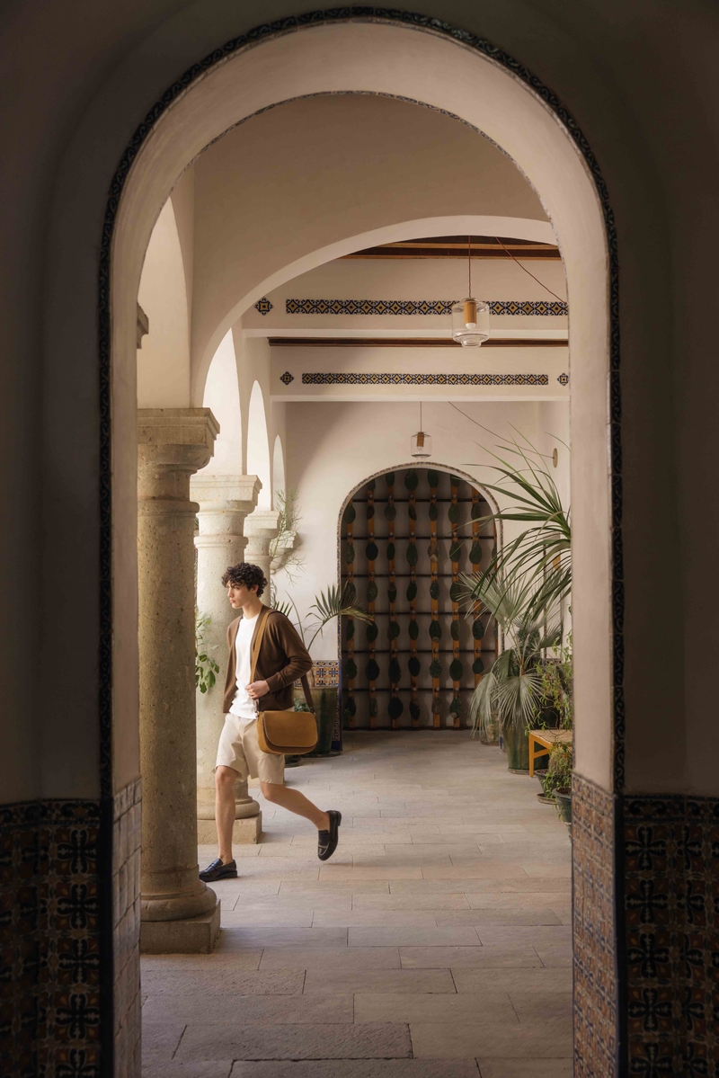 Wandering through an arched hall, Maximillian Gabriel carries Métier’s Hunter messenger, exuding effortless summer chic.