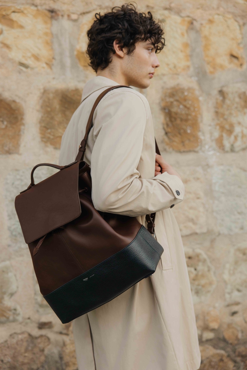 Against a stone wall, Maximillian Gabriel dons Métier’s sophisticated brown and black leather Glide backpack.