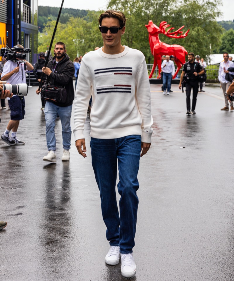 George Russell wears a Tommy Hilfiger flag sweater with jeans and white sneakers.