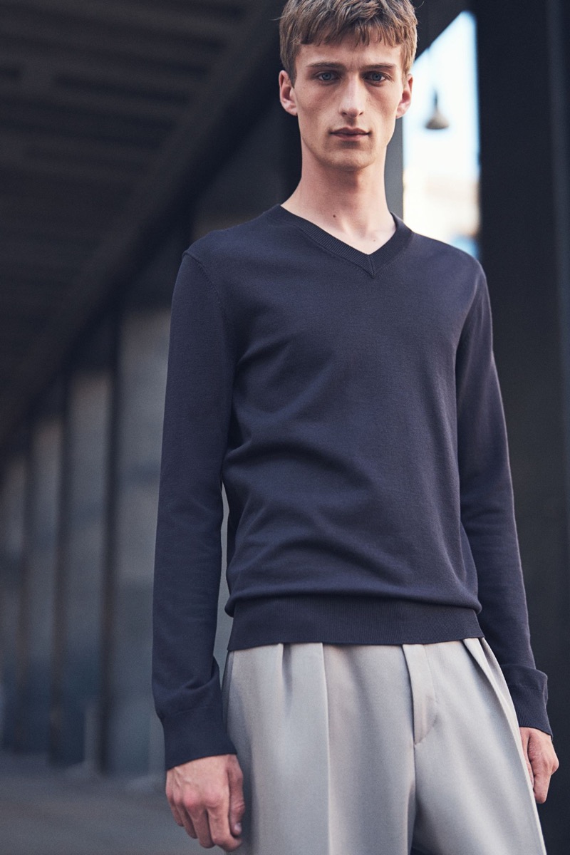 Model Vasko Luyckx wears a V-neck sweater with pleated trousers. 