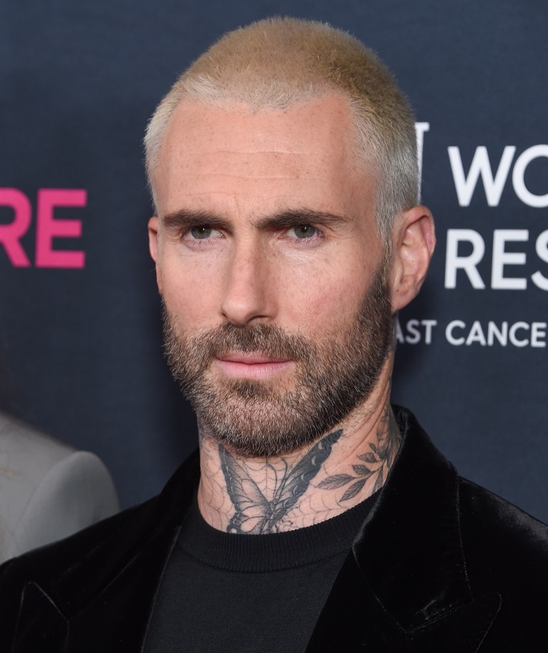 Adam Levine rocks a sharp platinum buzz cut paired with a dark beard, creating an effortlessly cool contrast.