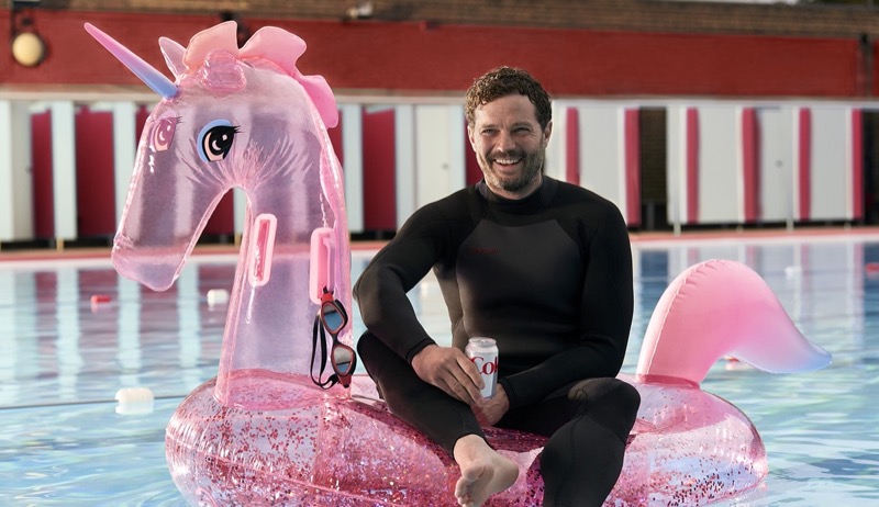 All smiles, Jamie Dornan is pictured on a unicorn floatie for his new Diet Coke commercial. 